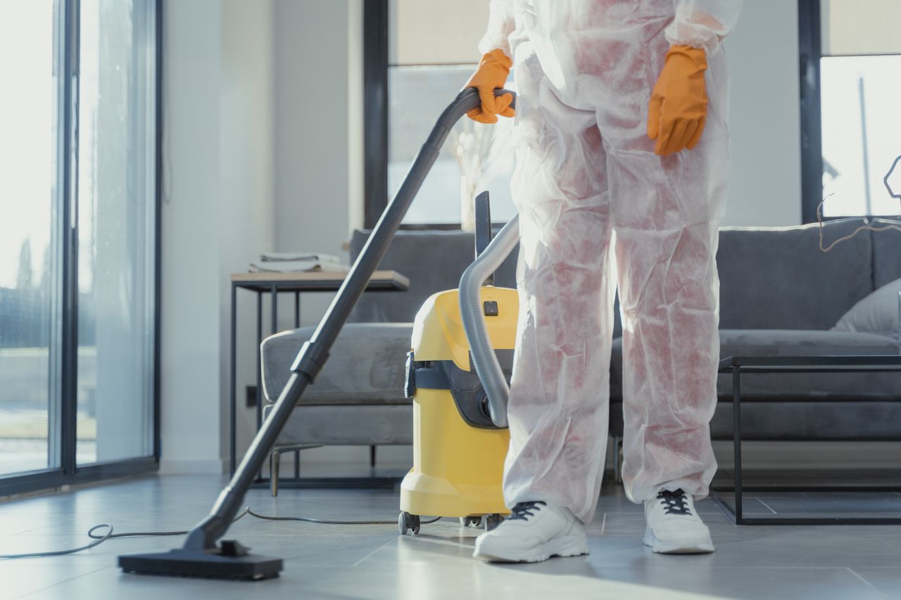 why-choose-us A cleaner in protective coveralls and gloves vacuuming a modern living room.