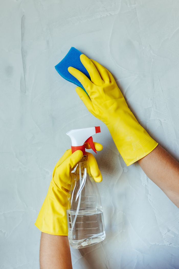 about-01 Hands in yellow gloves cleaning wall with sponge and spray bottle.
